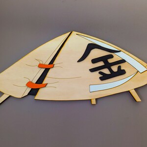 May include: A wooden cutout of a conical hat with orange straps and the Chinese character for "gold" written in black on the front.