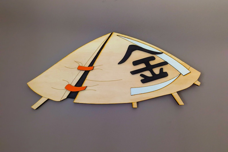 May include: A wooden cutout of a conical hat with orange straps and the Chinese character for "gold" written in black on the front.