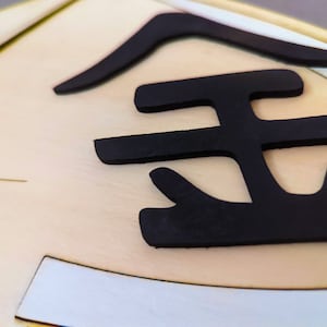 May include: Close-up of a gold-colored plaque with a black, raised, stylized Japanese character for "gold" on it.