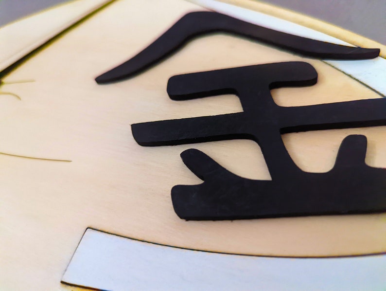 May include: Close-up of a gold-colored plaque with a black, raised, stylized Japanese character for "gold" on it.