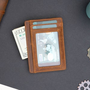May include: A brown leather wallet with a card slot and a billfold. The wallet is open and has a credit card and cash inside.
