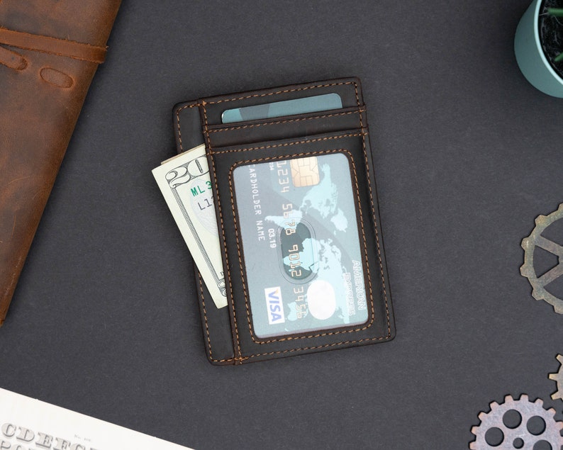 May include: A brown leather wallet with a stitched edge, holding a credit card and a dollar bill. The credit card has the Visa logo and the text "CARDHOLDER NAME".