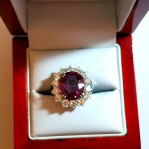 May include: A ring with a large oval-shaped pink gemstone surrounded by smaller diamonds in a white gold setting. The ring is in a red velvet ring box.