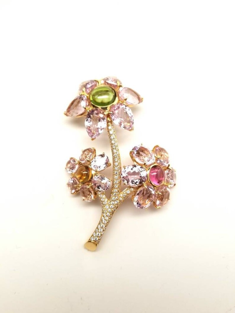 May include: A gold flower brooch with pink, green, and yellow gemstones. The brooch is made of 14k gold and features a delicate stem with diamond accents.