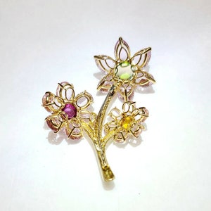 May include: A gold brooch with three flowers made of pink, green, and yellow gemstones. The flowers are connected by a gold stem.