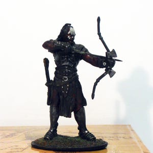 Puede incluir: Una figura de guerrero Orc negro y verde sosteniendo un arco y una flecha. La figura está de pie sobre una base marrón con un parche de hierba verde. La figura forma parte de una colección de El Señor de los Anillos. La caja tiene el texto "Lurtz at Parth Galen" y "Nr: 4.R" en ella.