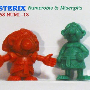 Op de afbeelding: Twee kleine Asterix-beeldjes. Eén is rood met uitgestrekte armen, de andere groen. De tekst "ASTERIX Numerobis & Misenplis" staat boven de beeldjes en "AX68 NUMI -18" eronder.
