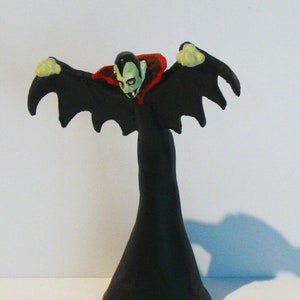 May include: A black plastic vampire figurine with red and white accents. The vampire has a cape and wings and is in a flying pose.