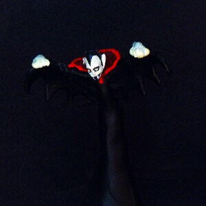 May include: A black and red vampire figurine with outstretched arms and a cape. The figurine is standing on a black base.