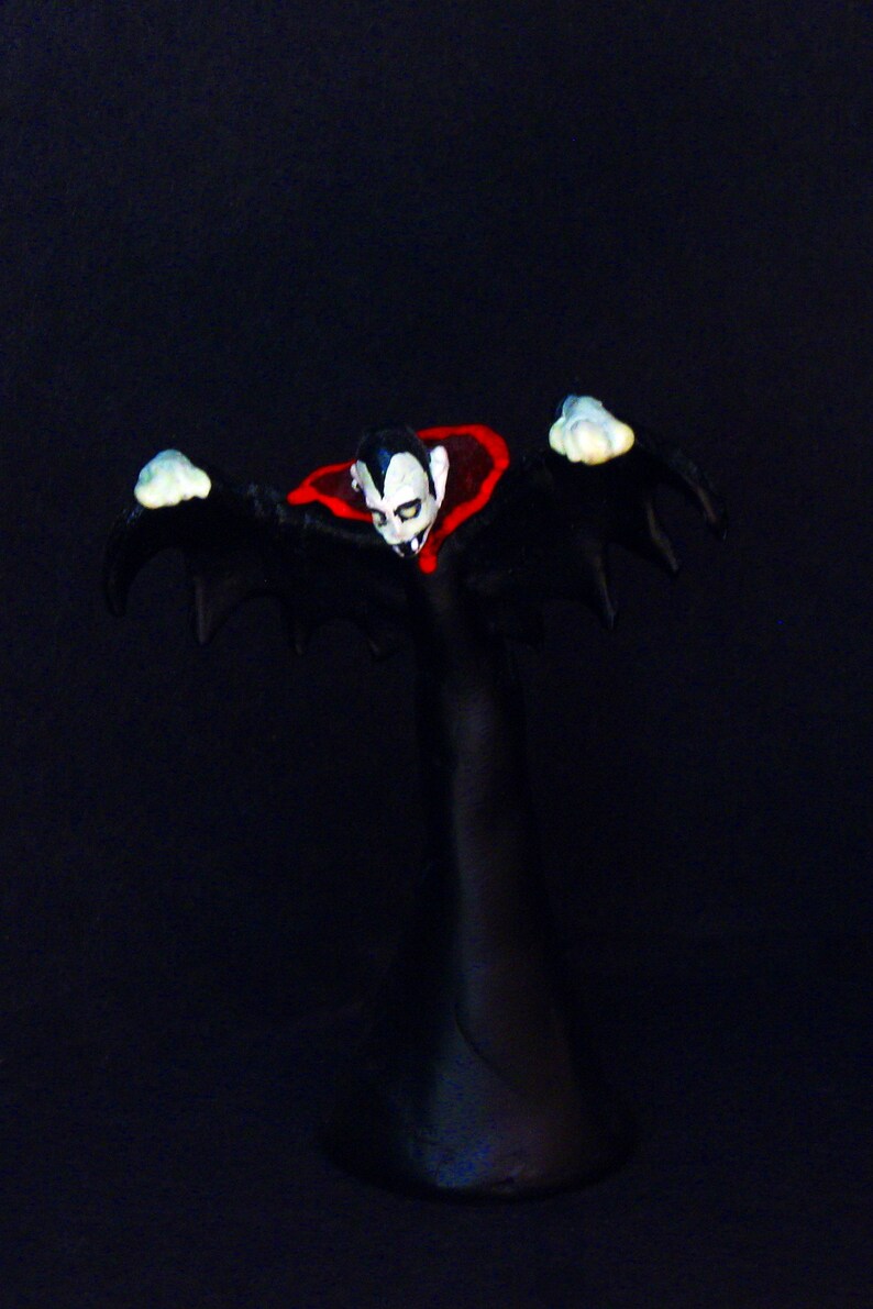 May include: A black and red vampire figurine with outstretched arms and a cape. The figurine is standing on a black base.