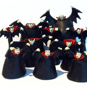 May include: A group of 11 black and red vampire figurines with wings outstretched. The figurines are arranged in a circle with one larger figurine in the centre.
