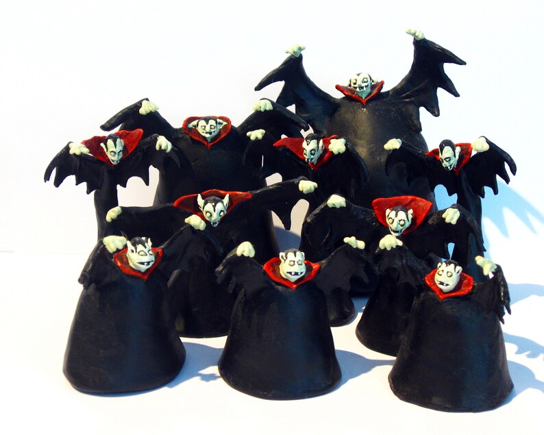 May include: A group of 11 black and red vampire figurines with wings outstretched. The figurines are arranged in a circle with one larger figurine in the centre.