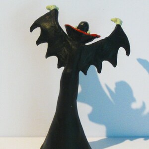 May include: A black and red plastic figurine of a vampire with outstretched wings. The vampire is wearing a black cape and a red hat.