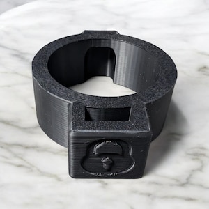 May include: A black plastic 3D printed ring with a padlock design. The ring has a large opening in the center.