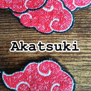 Op de afbeelding: Geborduurde patches met een rood wolkontwerp, witte wervelingen en een zwarte omtrek. Het woord "Akatsuki" wordt weergegeven in witte blokletters. Deze patches zijn geschikt voor kleding of accessoires.