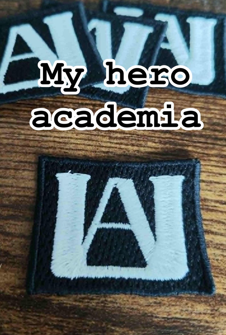 Może przedstawiać: Czarne, haftowane naszywki z napisem "My hero academia" i literami "UA" w kolorze białym. Prostokątne naszywki mają czarną obw&oacute;dkę i są umieszczone na drewnianej powierzchni.