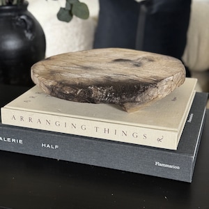 May include: A rustic wooden round serving tray sits on top of two books. The top book is titled "Arranging Things" and the bottom book is titled "Galerie Half" by Flammarion.