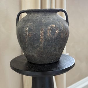 May include: A black ceramic vase with gold lettering that reads "PION" sits on a black pedestal.