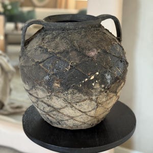 May include: A dark gray ceramic vase with two handles and a woven pattern. The vase has a rustic, aged look.