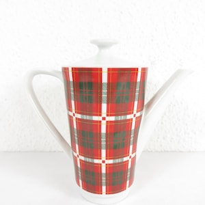 May include: A white ceramic teapot with a red, green, and yellow plaid pattern. The teapot has a long spout, a curved handle, and a lid with a small knob. The teapot is designed for serving tea.