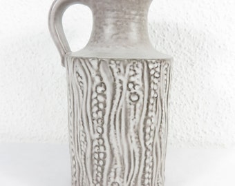 May include: A gray ceramic pitcher with a handle and a textured surface. The pitcher has a cylindrical body with vertical, textured patterns and a small spout. The overall design is simple and elegant.