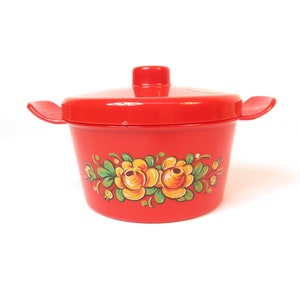 Peut inclure: Pot en plastique rouge avec un couvercle et un motif floral. Le pot a un fond blanc avec des fleurs jaunes et vertes.