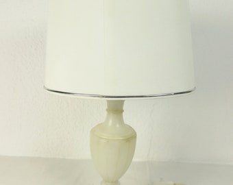 Peut inclure: Une lampe de table en albâtre blanc avec un abat-jour en tissu blanc et une bordure argentée. La lampe a un design classique avec une base ronde et un corps haut et fin.