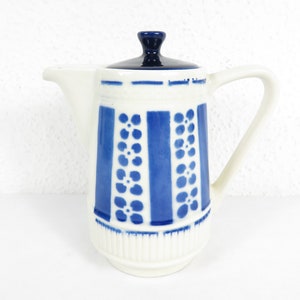 May include: A white ceramic creamer with a blue and white floral pattern. The creamer has a lid with a blue top.