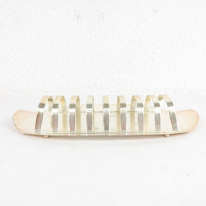 Puede incluir: Rebanador de pan de metal plateado con seis ranuras curvas y una base rectangular. El rebanador está diseñado para sostener barras de pan.