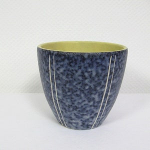 Può includere: Un piccolo vaso in ceramica blu con un bordo giallo e linee bianche. Il vaso ha una texture macchiettata.