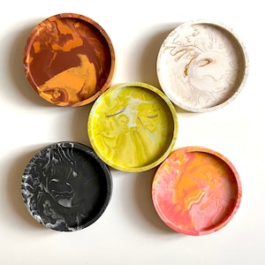 Pu&ograve; includere: Cinque sottobicchieri rotondi con un designo marmoreo. I sottobicchieri sono di vari colori, tra cui nero, bianco, giallo, arancione e marrone.