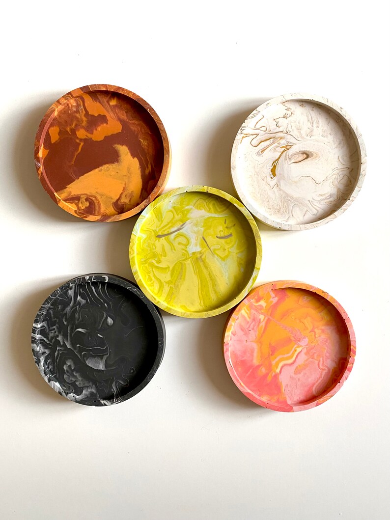 Pu&ograve; includere: Cinque sottobicchieri rotondi con un designo marmoreo. I sottobicchieri sono di vari colori, tra cui nero, bianco, giallo, arancione e marrone.