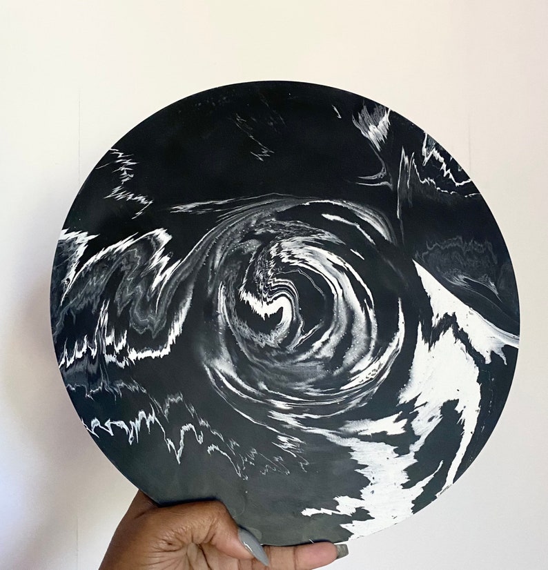 Pu&ograve; includere: Un vassoio circolare nero e bianco con un motivo a spirale di marmo. Il vassoio &egrave; realizzato in resina e ha una finitura liscia e lucida.
