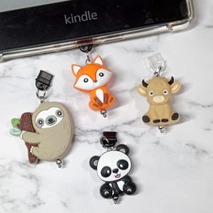 May include: Four colorful animal-shaped book markers with silver clips. The markers are a sloth, a fox, a panda, and a cow. The markers are hanging from a black Kindle e-reader.