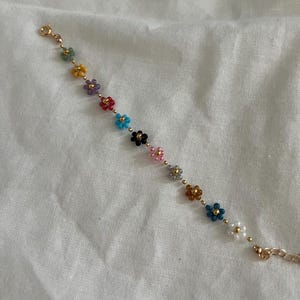 May include: A gold chain bracelet with small colorful flower-shaped beads. The bracelet has a clasp closure.