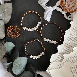 Könnte beinhalten: Drei Perlenarmbänder mit weißen Buchstabenperlen, die "BOOKWORM", "BOOKS" und "READER" buchstabieren. Die Armbänder sind aus braunen, goldenen und weißen Perlen gefertigt.
