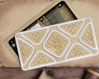 May include: A wooden sewing box with a decorative lid, open to reveal needles and pins, sits on a wooden surface. Antique scissors, spools of thread, buttons, and lace are arranged around the box, suggesting a crafting theme.