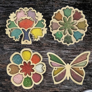 Könnte beinhalten: Vier Holztabletts in verschiedenen Formen, die jeweils mit bunten Perlen gefüllt sind. Die Formen sind ein Baum, eine Blume, ein Schmetterling und ein Kreis.