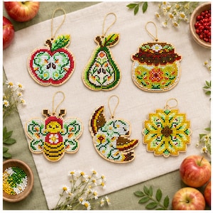 May include: Six wooden ornaments featuring cross-stitch patterns of an apple, a pear, a jar of preserves, a bee, a bird, and a sunflower. Each ornament has a gold string loop for hanging and displays intricate, colorful beadwork designs.
