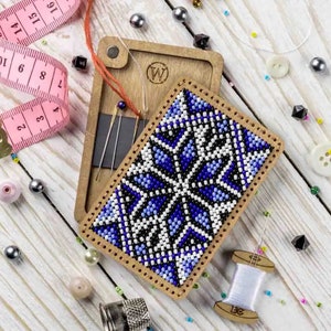 May include: A wooden box with a blue and white beaded design on the front. The box is open and contains needles and a small spool of thread. The box is surrounded by beads and a pink measuring tape.
