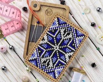 May include: A wooden box with a blue and white beaded design on the front. The box is open and contains needles and a small spool of thread. The box is surrounded by beads and a pink measuring tape.