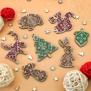 May include: A set of eight wooden Christmas ornaments with various designs, including a reindeer, a tree, a squirrel, a mushroom, a bunny, an acorn, and two trees. The ornaments are decorated with colorful beads and sequins.