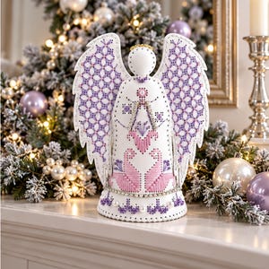 May include: A white angel figurine featuring intricate purple and pink cross-stitch embroidery on its wings and body. The design includes two pink birds at the base, a gold halo, and decorative pearl and crystal accents along the hem and center.