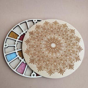 May include: A wooden craft organizer with a circular design. The organizer has a segmented interior filled with colorful beads. The lid features an intricate, engraved mandala pattern. The color palette includes natural wood tones and vibrant bead colors.