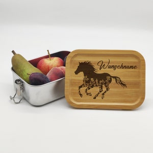 Könnte beinhalten: Eine Edelstahl-Lunchbox mit einem Bambusdeckel. Der Deckel hat eine Silhouette eines Pferdes mit floralen Details und dem Text "Wunschname". Die Lunchbox ist mit Obst gefüllt, darunter eine Birne, ein Apfel und Pfirsiche.