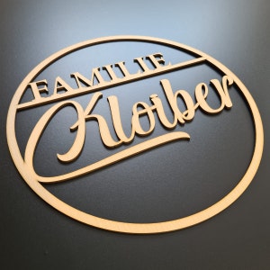 Könnte beinhalten: Ein rundes Holzschild mit dem Text "Familie Kloiber" in einer dekorativen Schrift.