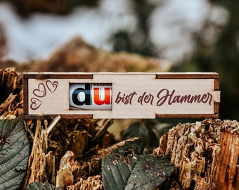 Può includere: Una scatola di legno con una piccola finestra che dice "du" all'interno. La scatola è decorata con tre cuori e il testo "du bist der Hammer".