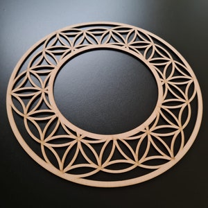 Könnte beinhalten: Ein kreisförmiges Holzdekorationsstück mit einem geometrischen Muster. Die natürliche Holzfarbe kontrastiert mit dem dunklen Hintergrund. Das Design ist offen, mit negativem Raum, der einen spitzenartigen Effekt erzeugt. Durchmesser ca. 20 cm.