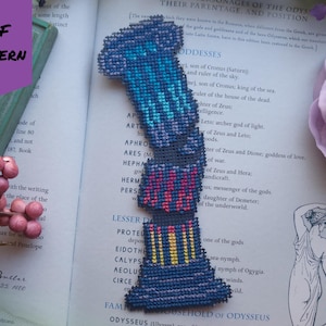 May include: A cross-stitch bookmark in a column design, with blue, pink, and yellow hues. The bookmark is on an open book with text and a purple flower. The words "PDF PATTERN" are in a purple banner. The bookmark is likely a craft item.