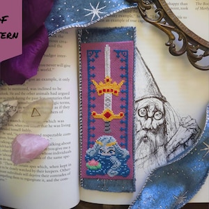 May include: A cross-stitch bookmark with a sword and crown design, featuring a blue bunny with a flower. The bookmark is on a book with a wizard illustration and the text "PDF PATTERN". The bookmark is approximately 20 cm long.